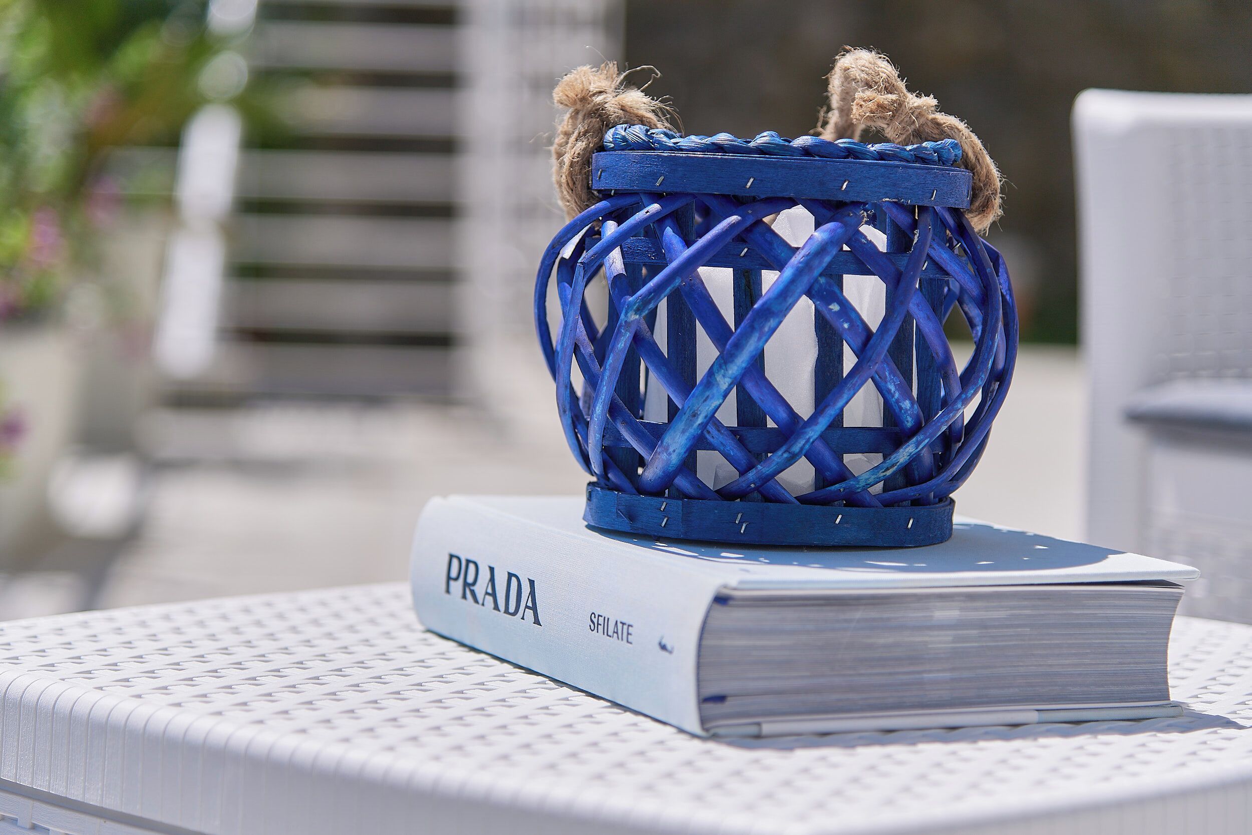 A blue woven basket with twine on top of a white book titled "PRADA" on a white chair.