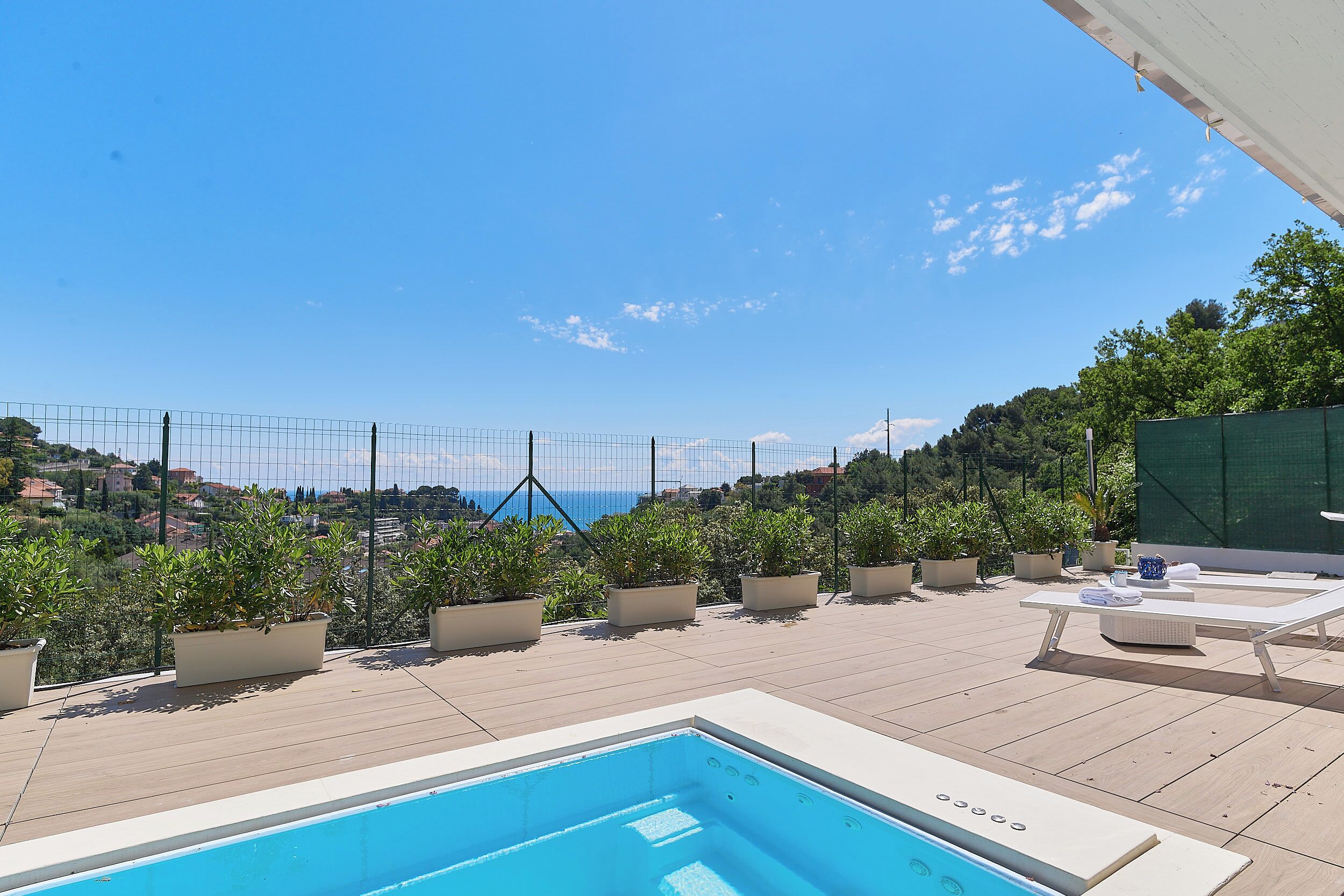 Zona de piscina en la azotea con vista despejada al mar, rodeada de plantas en macetas y sillones de descanso.