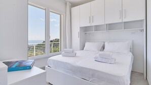 A modern bedroom with a large bed, white bedding, and a view of the sea through a large window. - The Italian Lady (Alassio)