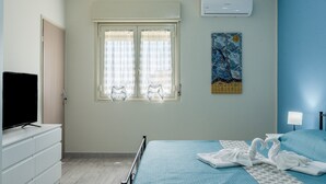 A bedroom with a bed, a television, a window with curtains, and a painting on the wall. - Villa 'La Conchiglia' with Wi-Fi and Air Conditioning (Licata)