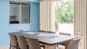A dining area with a table and chairs, a hanging net decoration, a view through a window, and a door leading outside. - Villa 'La Conchiglia' with Wi-Fi and Air Conditioning (Licata)