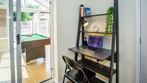 A room with a pool table, a desk with a laptop, a chair, and a bookshelf with books and a sign that says "BEYOND STAYS".