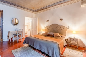 Une chambre à coucher comprenant un lit, des tables de chevet, une chaise, un miroir et une porte donnant sur une autre pièce.