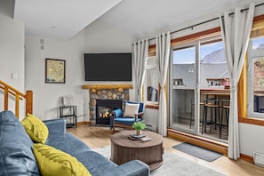 Een woonkamer met een stenen openhaard, een bank, een salontafel en een aan de muur bevestigde televisie.