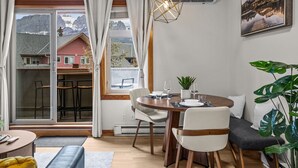 A dining area with a table set for two, a potted plant, and a view of mountains through large windows.