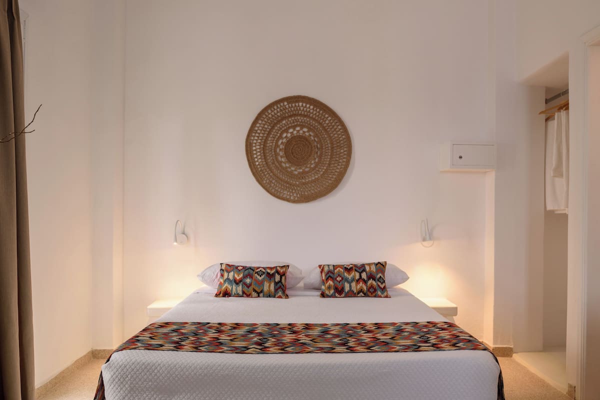 A neatly arranged bedroom with a bed, two pillows, a wall-mounted circular decoration, and a bedside table.