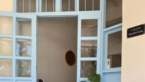 Un área de estar al aire libre con una mesa de madera y dos sillones, una planta en maceta y un cartel que indica la zona de recepción.