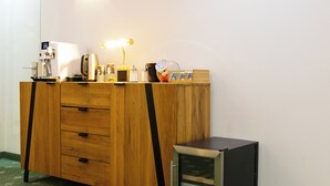 Uma mesa de madeira com cafeteira, luminária e uma pequena geladeira.