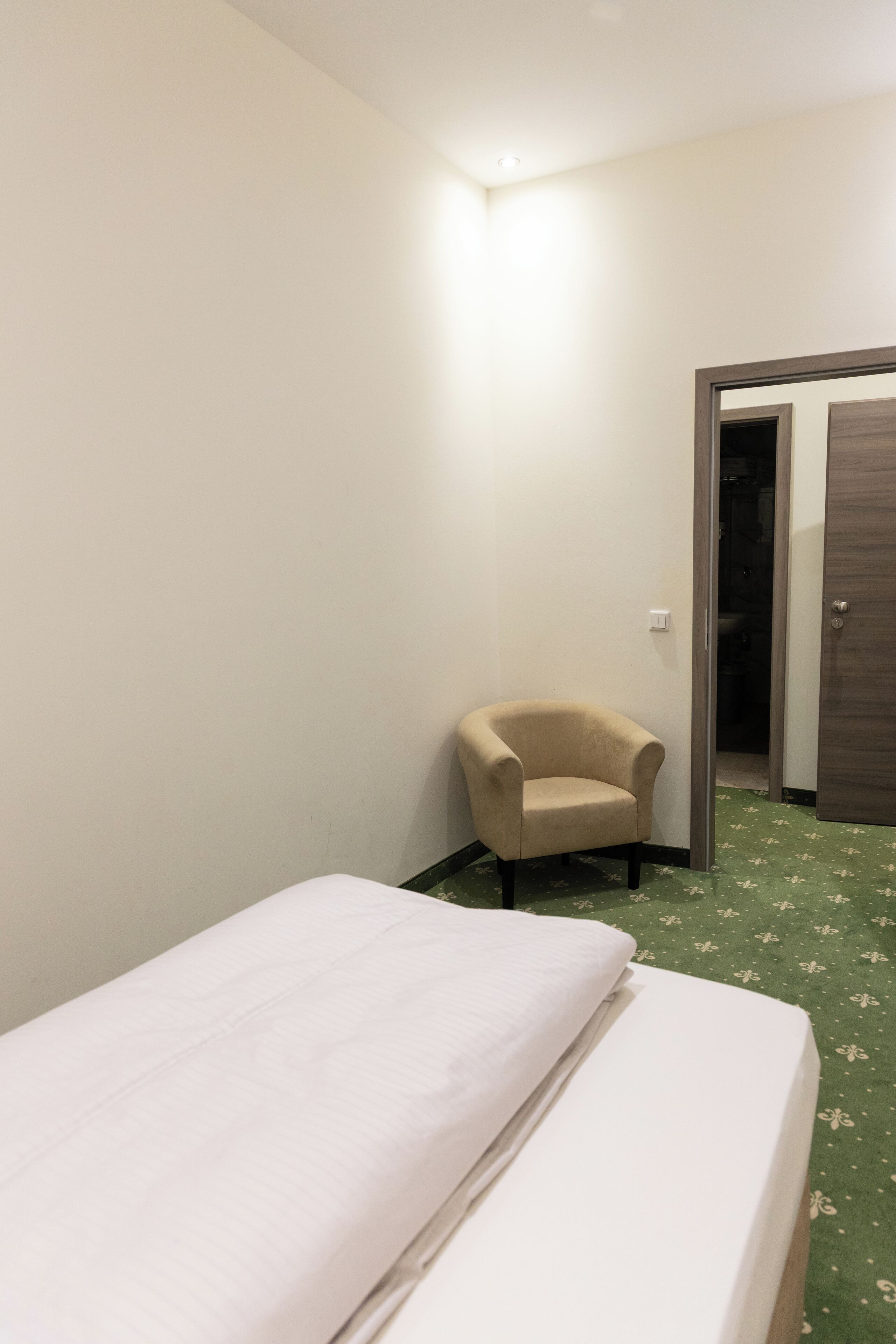 Una habitación pequeña y sencilla con una cama, una silla y una puerta que da a un baño.