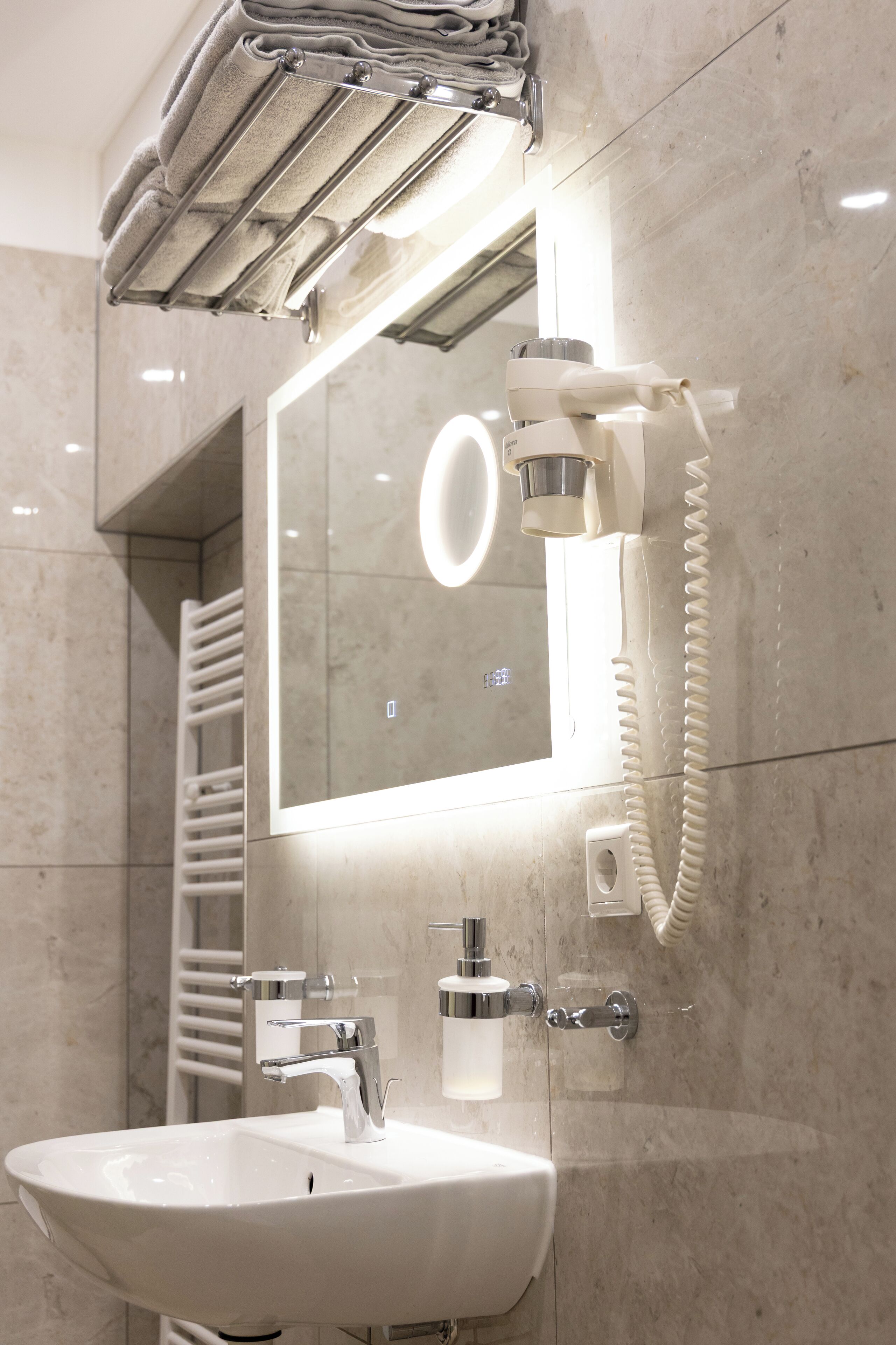 Un baño moderno con un lavamanos blanco, grifería cromada, un perchero y un espejo con luz integrada.