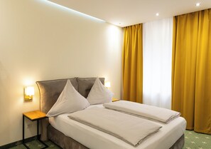 Habitación de hotel con cama doble, dos mesitas de noche con lámparas, cabecero y cortinas amarillas.
