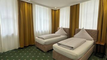 A hotel room with two beds, a green patterned carpet, and curtains.