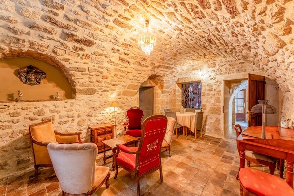 Una habitación con paredes de piedra, un candelabro, muebles de madera y una silla roja.