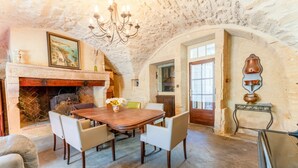 A dining area with a wooden table, chairs, a chandelier, a fireplace, and a stone wall. - The Jasmin suite has a shared swimming pool, Wi-Fi and air conditioning (Collias)