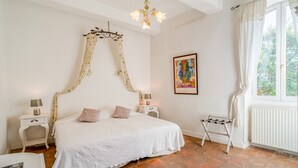 A bedroom with a large bed, two bedside tables, a hanging light fixture, a radiator, and a window with curtains. - The Jasmin suite has a shared swimming pool, Wi-Fi and air conditioning (Collias)