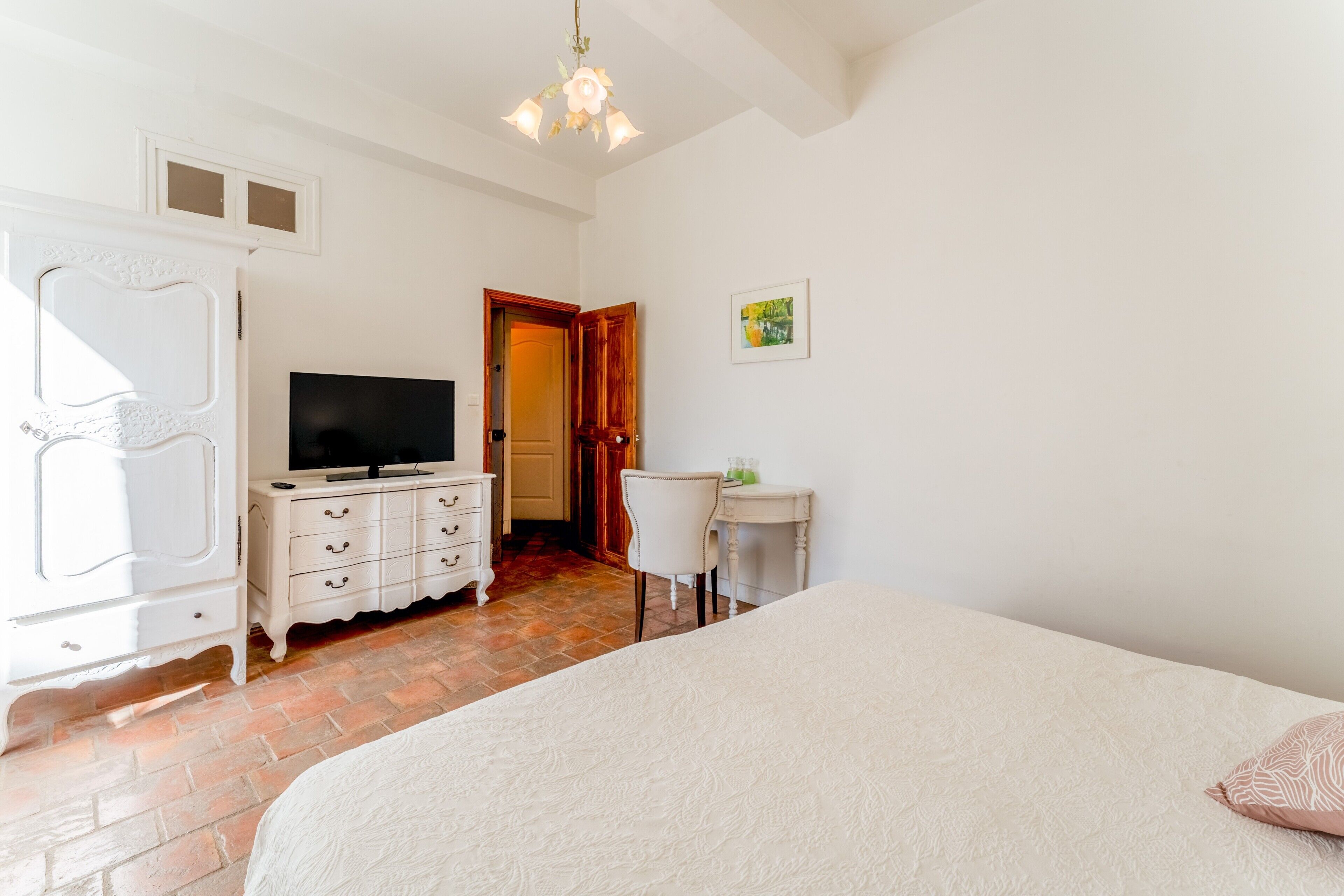 Un dormitorio con cama, televisión, cómoda, silla y una mesita.