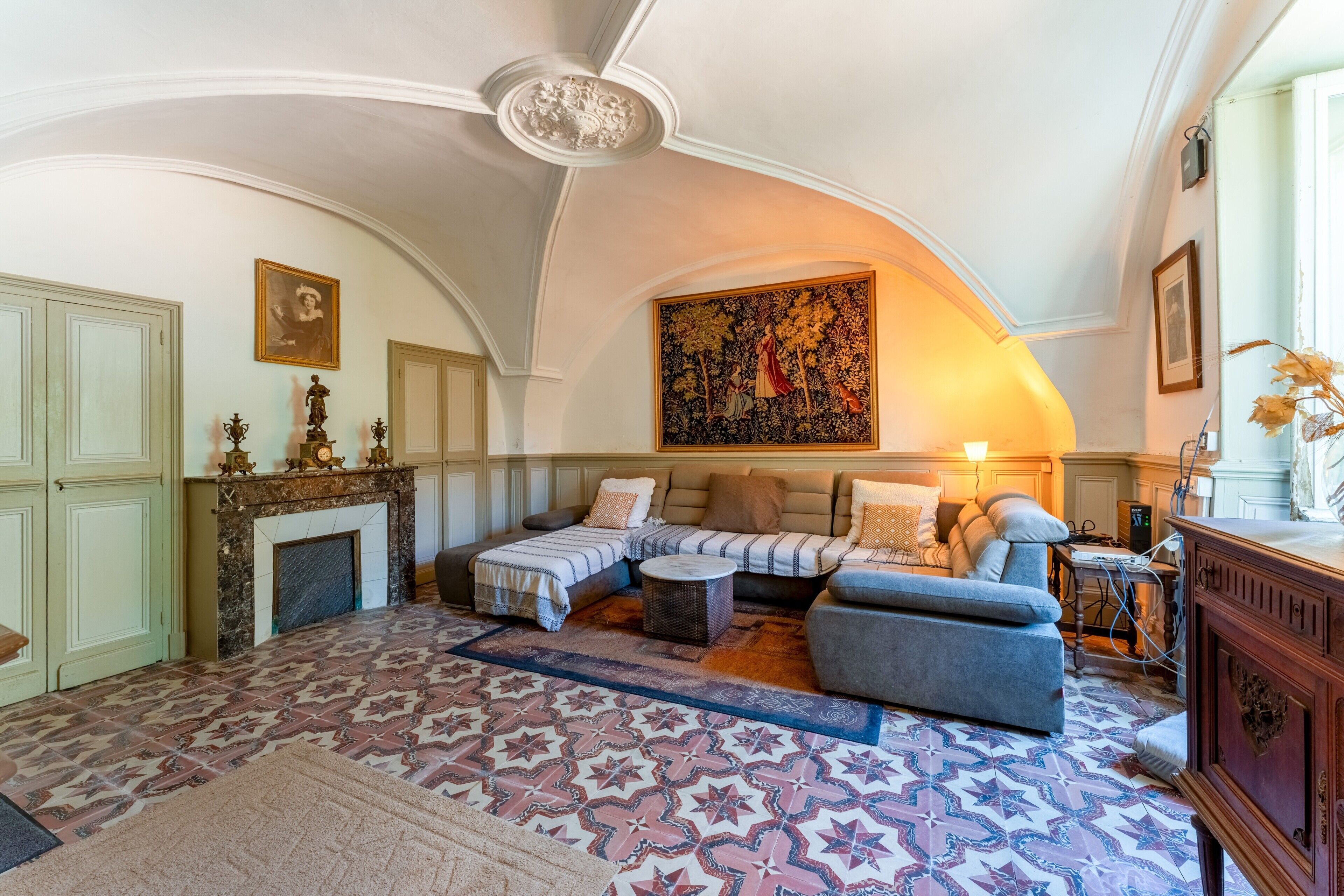 Una sala de estar con chimenea, un conjunto de sofás, un tapete estampado y un cuadro grande en la pared.