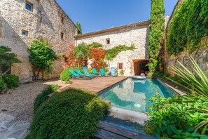 Ein Gebäude aus Stein mit Pool, Liegestühlen und viel Grün.