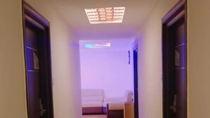 A narrow hallway with a carpeted floor leading to a room with a bed and a small table.