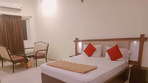 A hotel room with a bed, a chair, a nightstand, and an air conditioning unit.