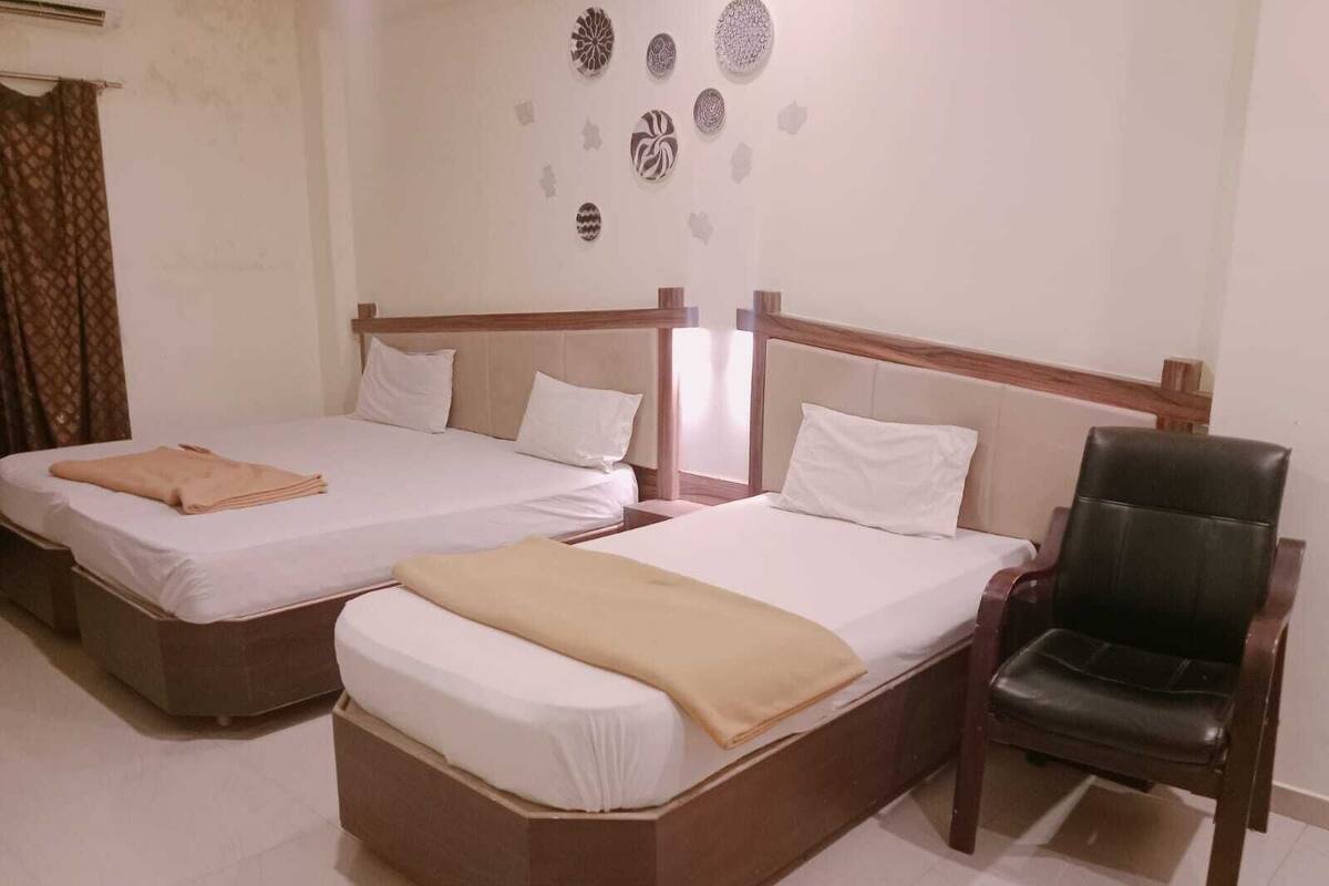 Hotellihuone, jossa on kaksi sänkyä, tuoli ja koristeellinen seinätaideteos.