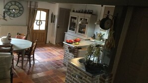 A kitchen with a checkered floor, a dining table with chairs, a clock on the wall, and a window with curtains.