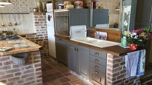 A kitchen with a brick wall, a wooden countertop, a sink, and a stove.