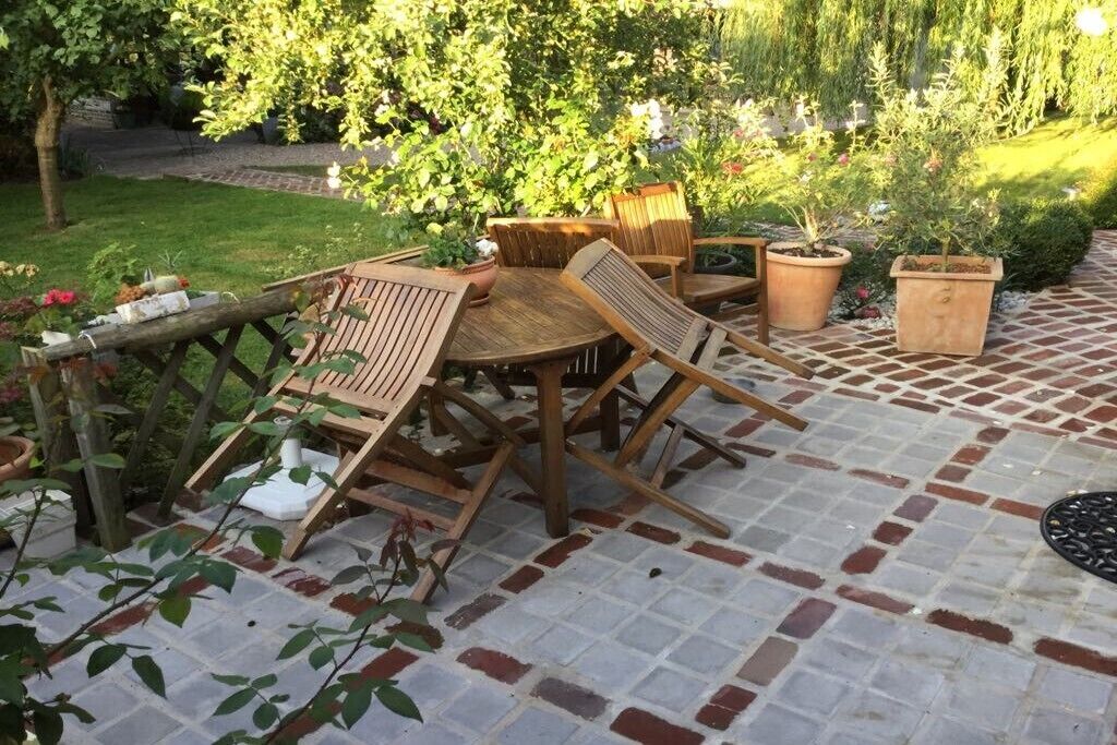 Un patio con tavolo e sedie in legno, circondato da piante in vaso e un pavimento in mattoni.