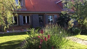 A brick house with a red tiled roof, a front porch, and a well-maintained garden with various plants and flowers.