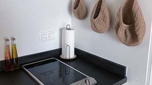 A kitchen with a black countertop, a built-in induction cooktop, two bottles of olive oil, and three woven hanging baskets on the wall.