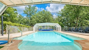 Una piscina con cerramiento de vidrio, rodeada por una valla y árboles.