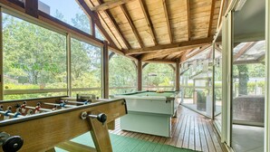 Mesa de billar y mesa de fútbolín en una habitación con ventanas amplias y vigas de madera.