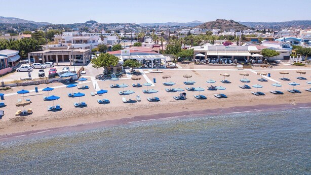 A beachside hotel with multiple lounge areas, a pool, and a view of the surrounding town. - Cactus Suites  (Faliraki)