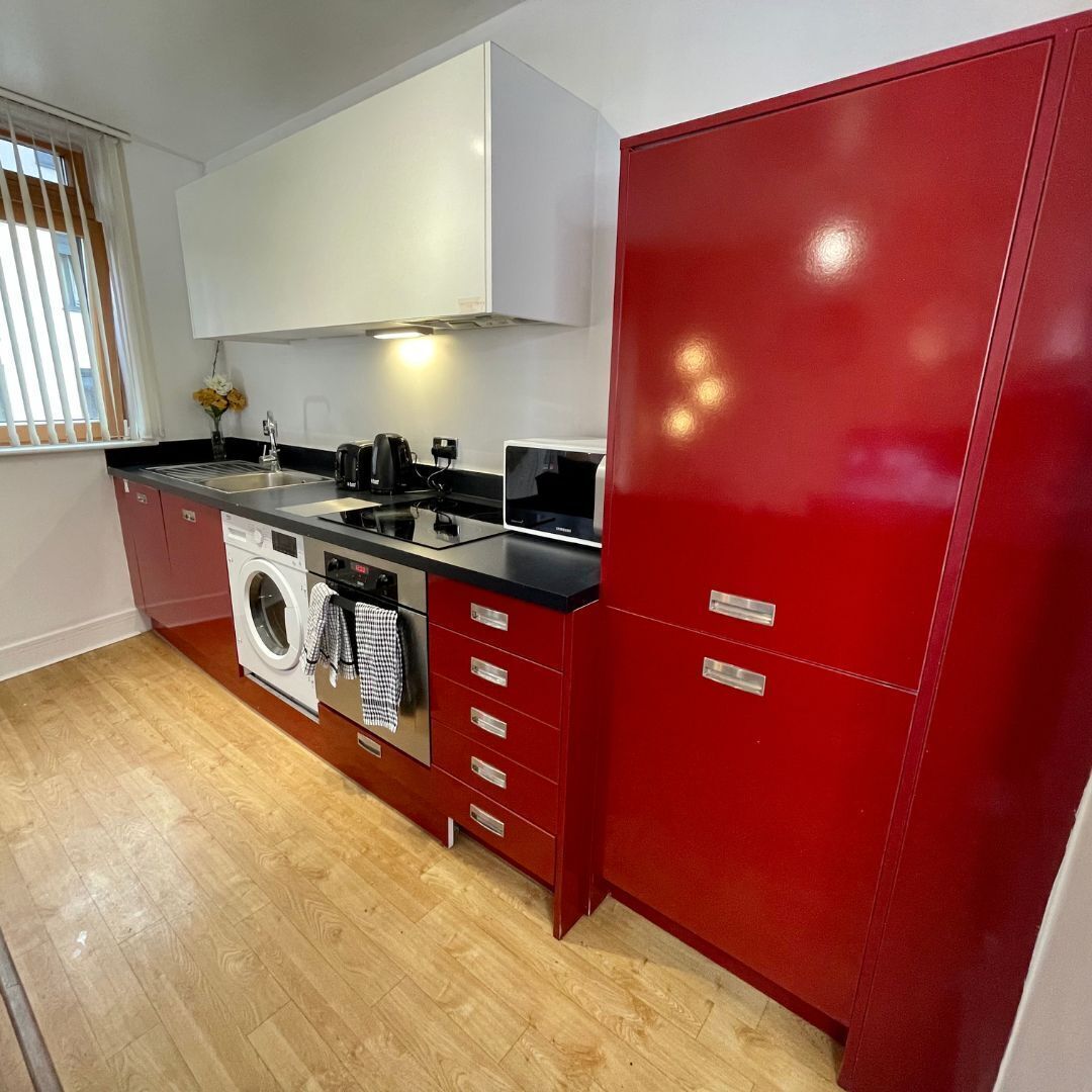 A compact kitchen with a washing machine, a microwave, and a red cabinet.