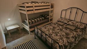 Ein Schlafsaal mit Etagenbetten, einem Schreibtisch, einem Heizkörper und einem Streifenmuster-Teppich.
