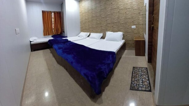 A hotel room with a bed, a nightstand, a window with curtains, and a door. - Hotel Shiv Ganga (Varanasi)