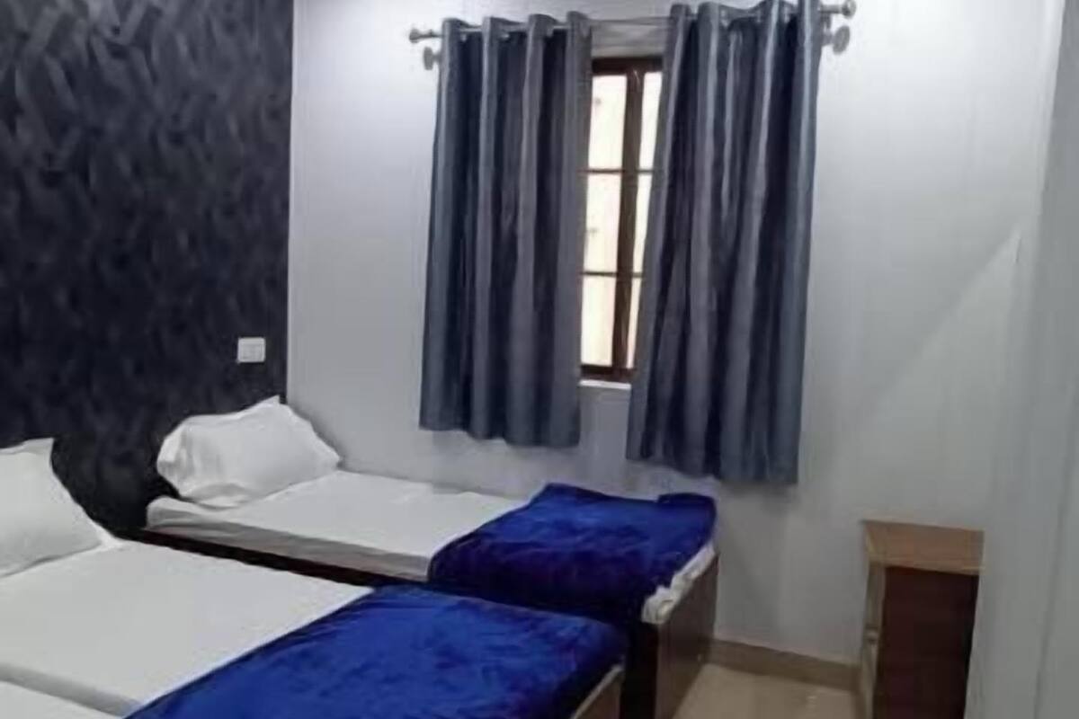 Una habitación con dos camas individuales, un ventilador de techo, una ventana con cortinas y una pequeña mesa de madera.