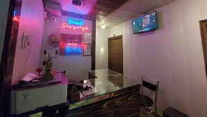 A reception area with a neon sign, a television, and a glass table with chairs. - Hotel Shiv Ganga (Varanasi)