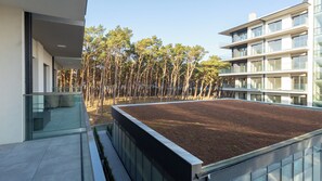 Un bâtiment moderne doté d’un jardin sur le toit, de rampes en verre et offrant une vue sur une forêt.