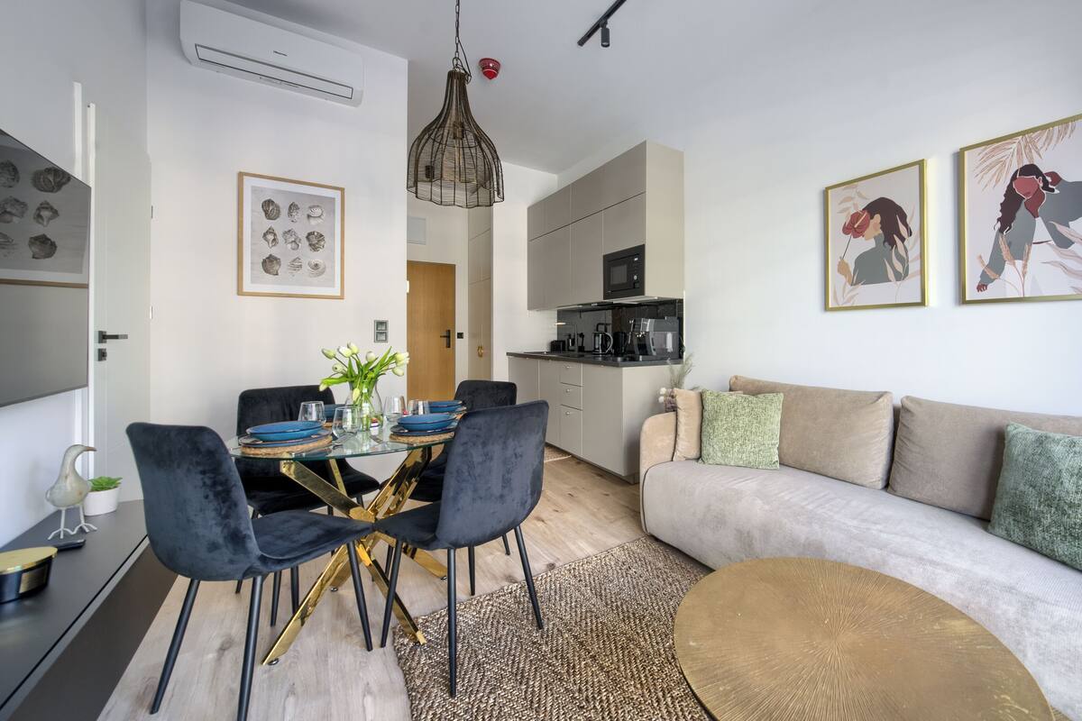 Een moderne woonkamer met een bank, eettafel en stoelen. Er is een keuken met een magnetron en kasten.