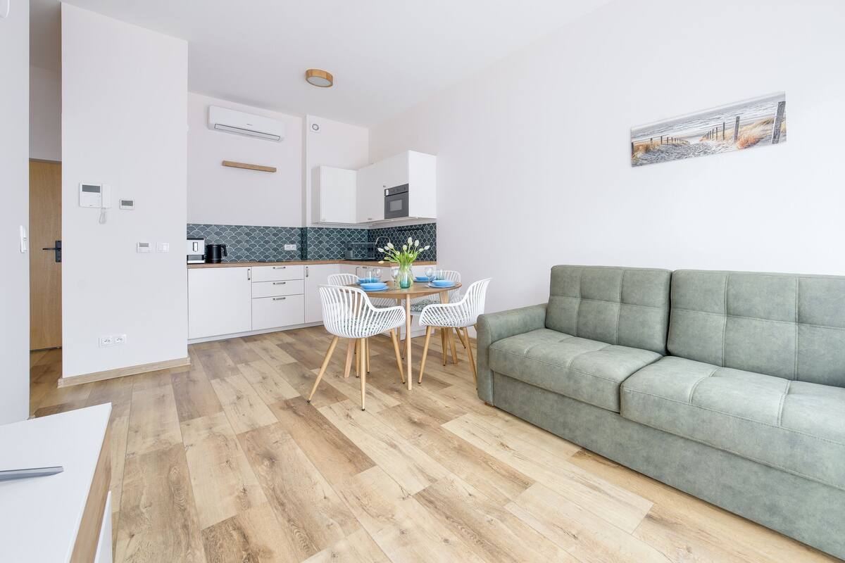 Een modern appartement met een eethoek, kitchenette en een grijze bank.