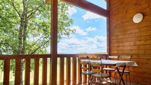 A wooden deck with a table and chairs, a view of trees and sky, and a wooden wall.