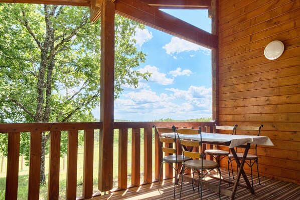 Una terraza de madera con una mesa y sillas, vistas a árboles y al cielo, y un muro de madera.