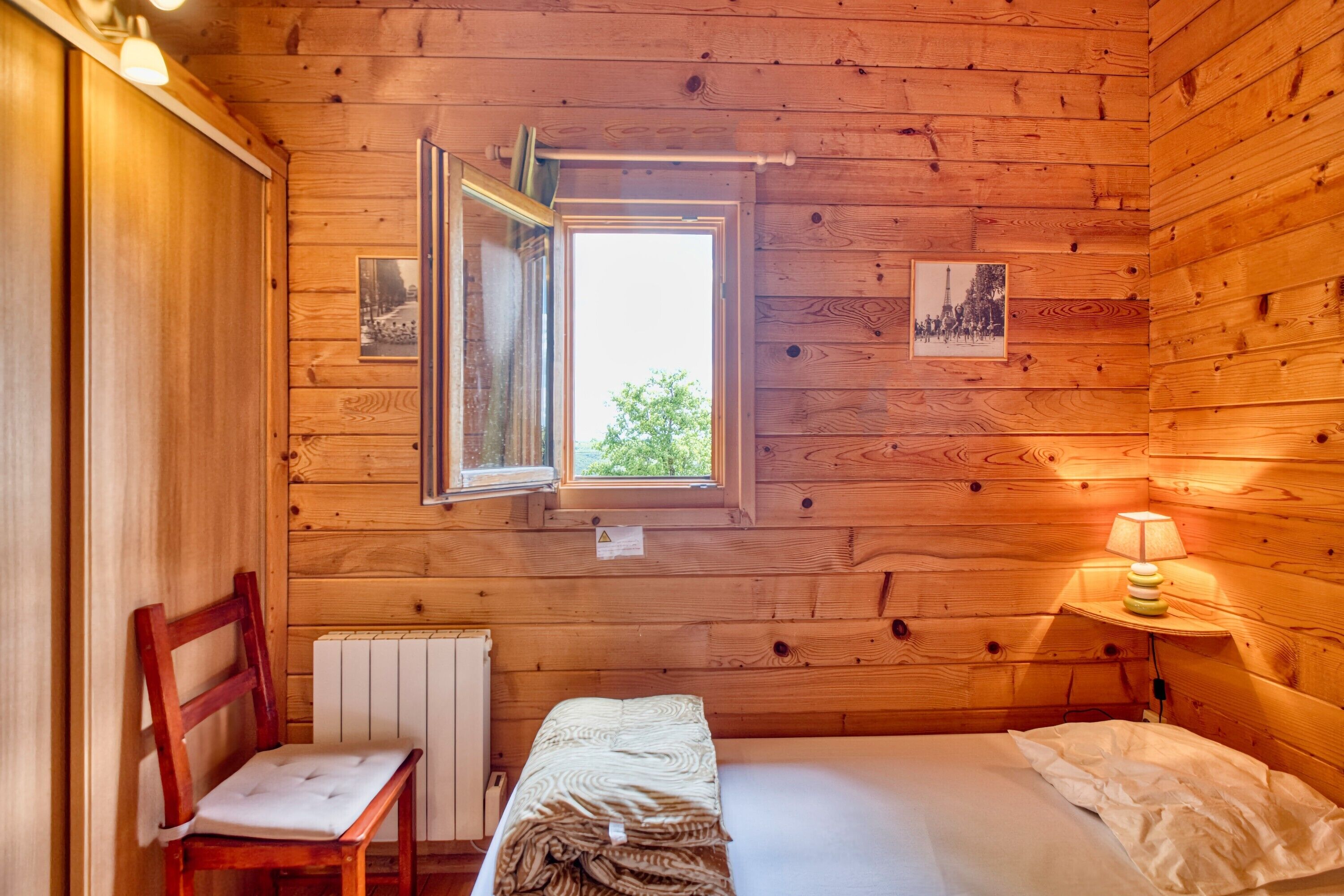 Una camera in una baita di legno con un letto, una sedia, una finestra e un comodino.