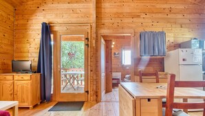 A wooden cabin interior with a dining table, chairs, a television, and a refrigerator.