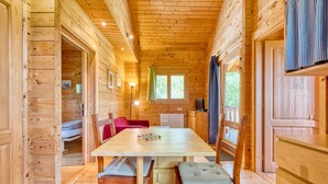 A wooden cabin interior with a dining table, chairs, a red sofa, and a window with curtains.