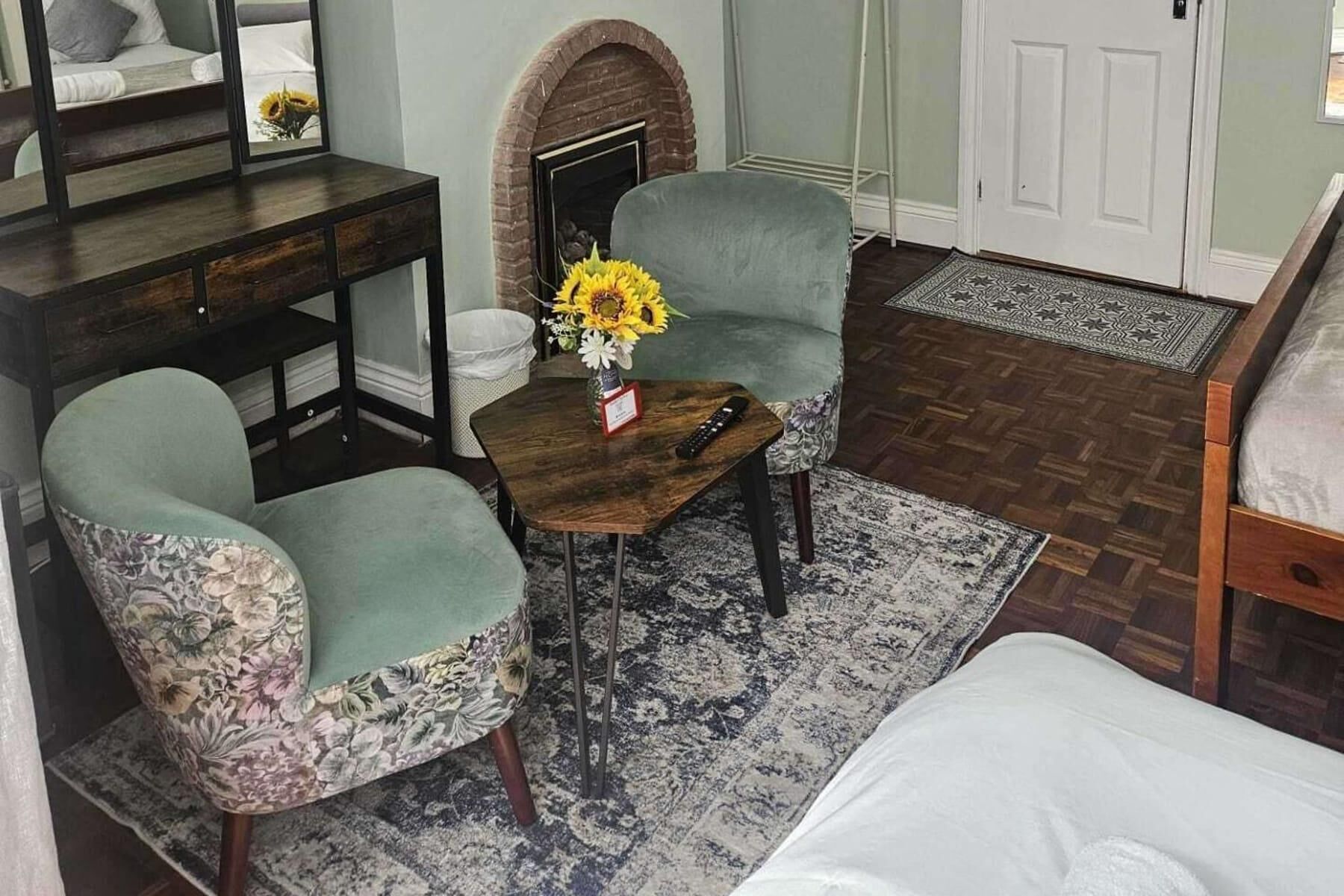 A cozy room with a fireplace, a sofa, a small table with a vase of sunflowers, and a patterned rug.