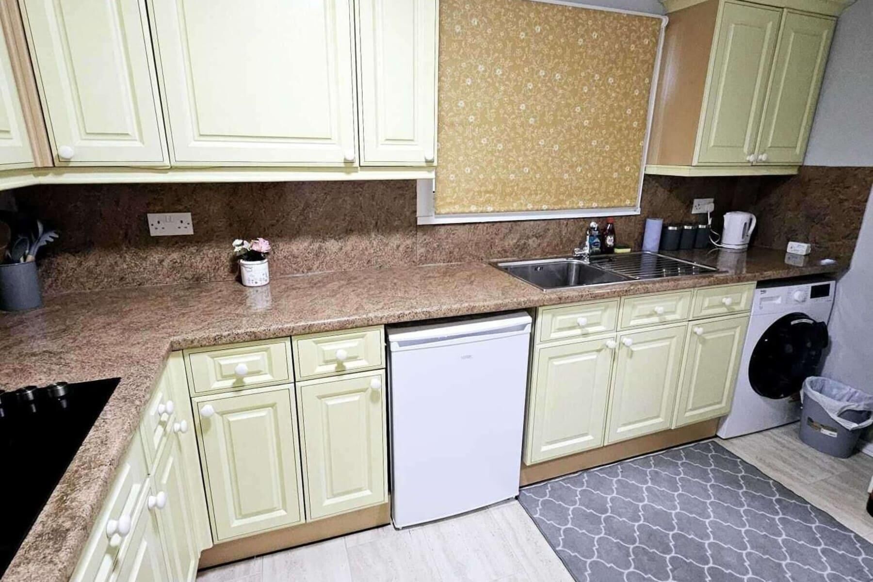 Una cocina con gabinetes verde claro, encimera de granito, lavavajillas y lavadora.