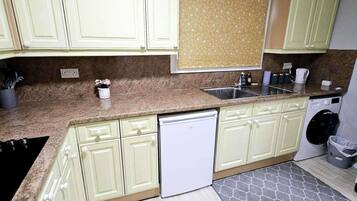 Una cocina con gabinetes verde claro, encimera de granito, lavavajillas y lavadora.