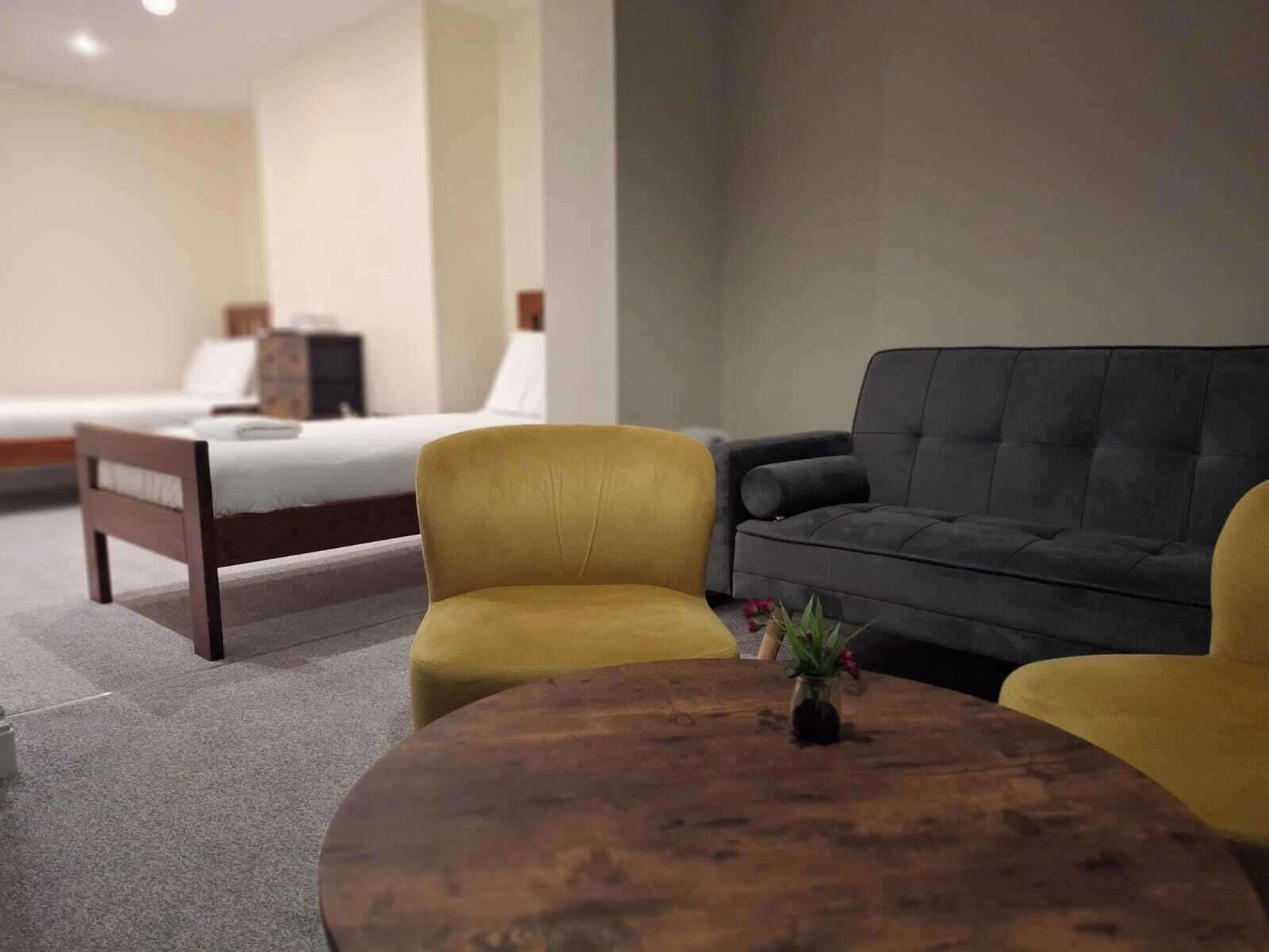 A hotel room with a bed, a sofa, a round wooden table, and a small plant.